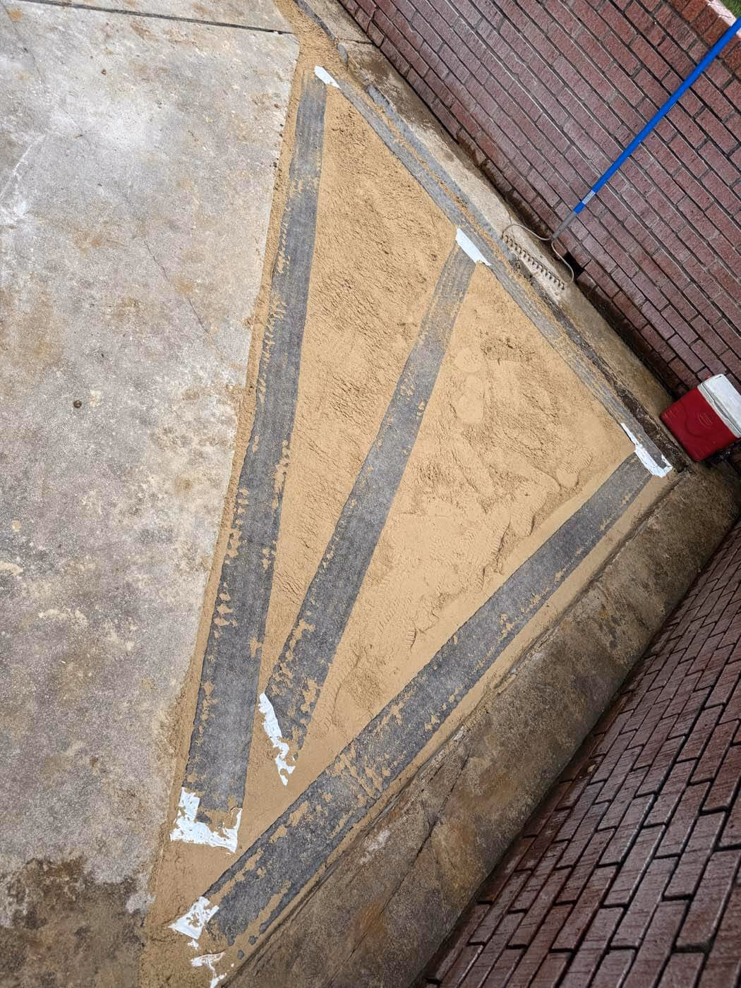 Concrete surface with two large triangular sections filled with sand, adjacent to a brick wall and a red cooler.