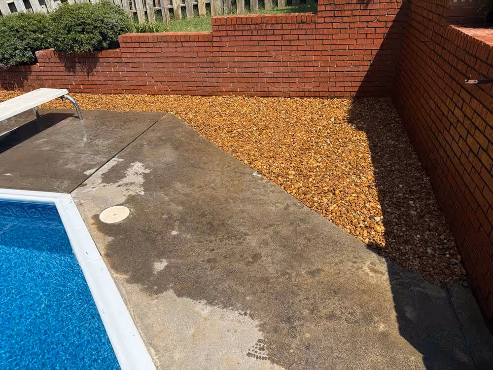 Backyard pool area with wet concrete deck, diving board, brick walls, and a rock garden section.